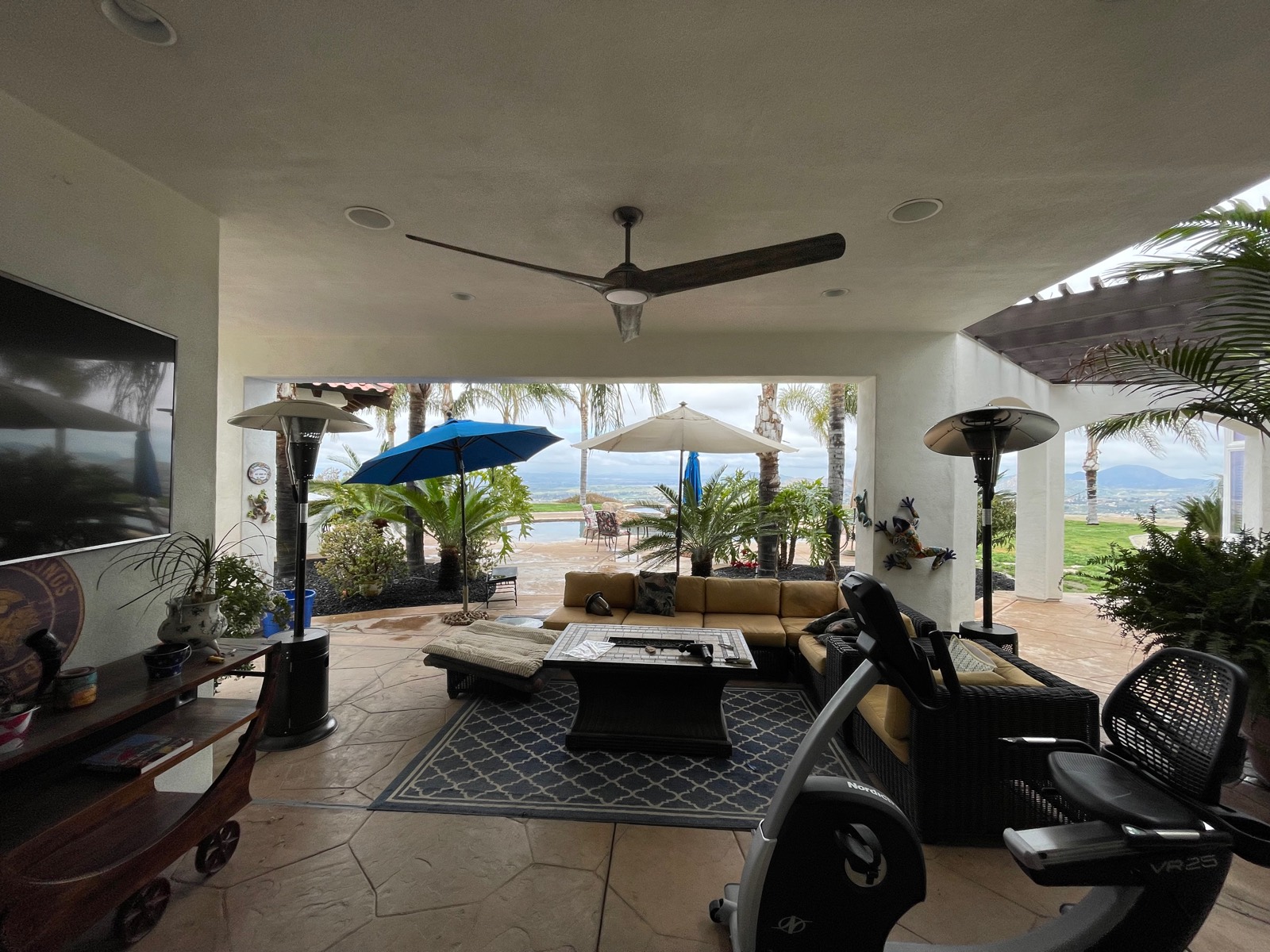 Large ceiling fan installed in a covered patio over an outdoor seating area, with patio heaters and a view to the yard