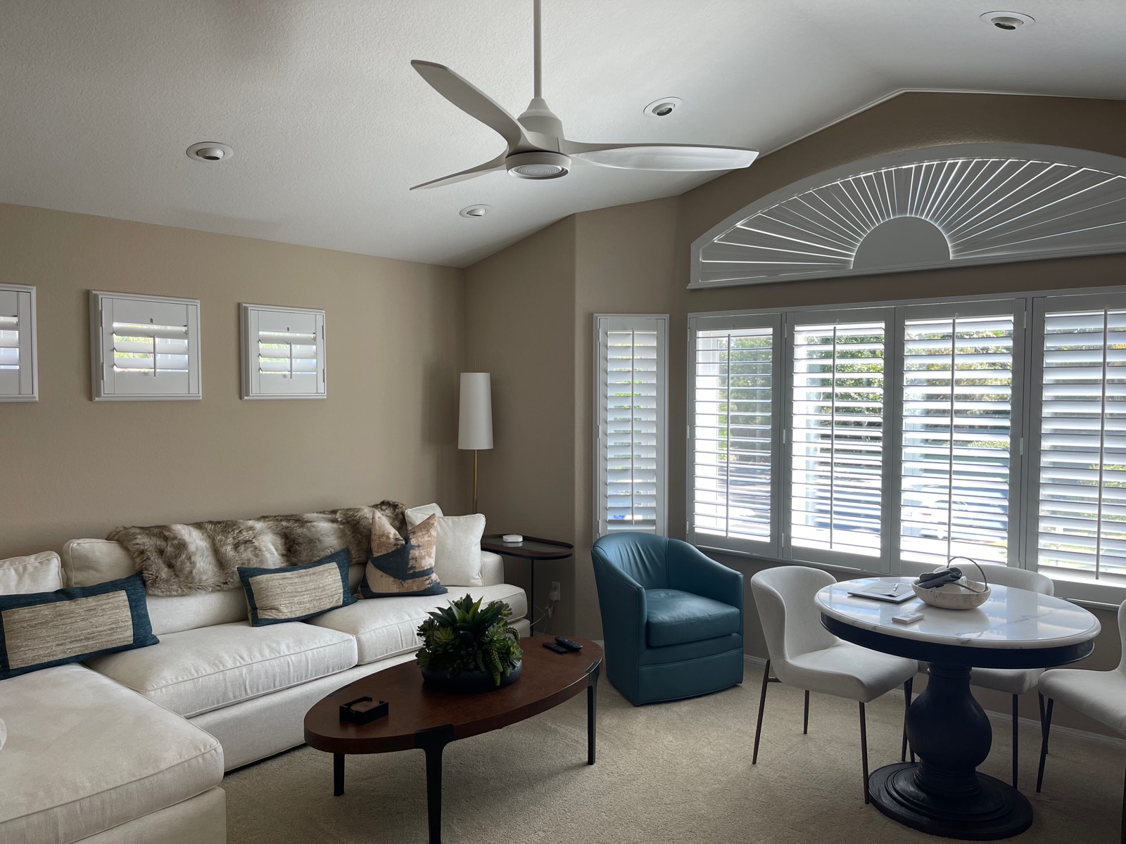 White three-blade ceiling fan with a light in a vaulted living room with plantation shutters