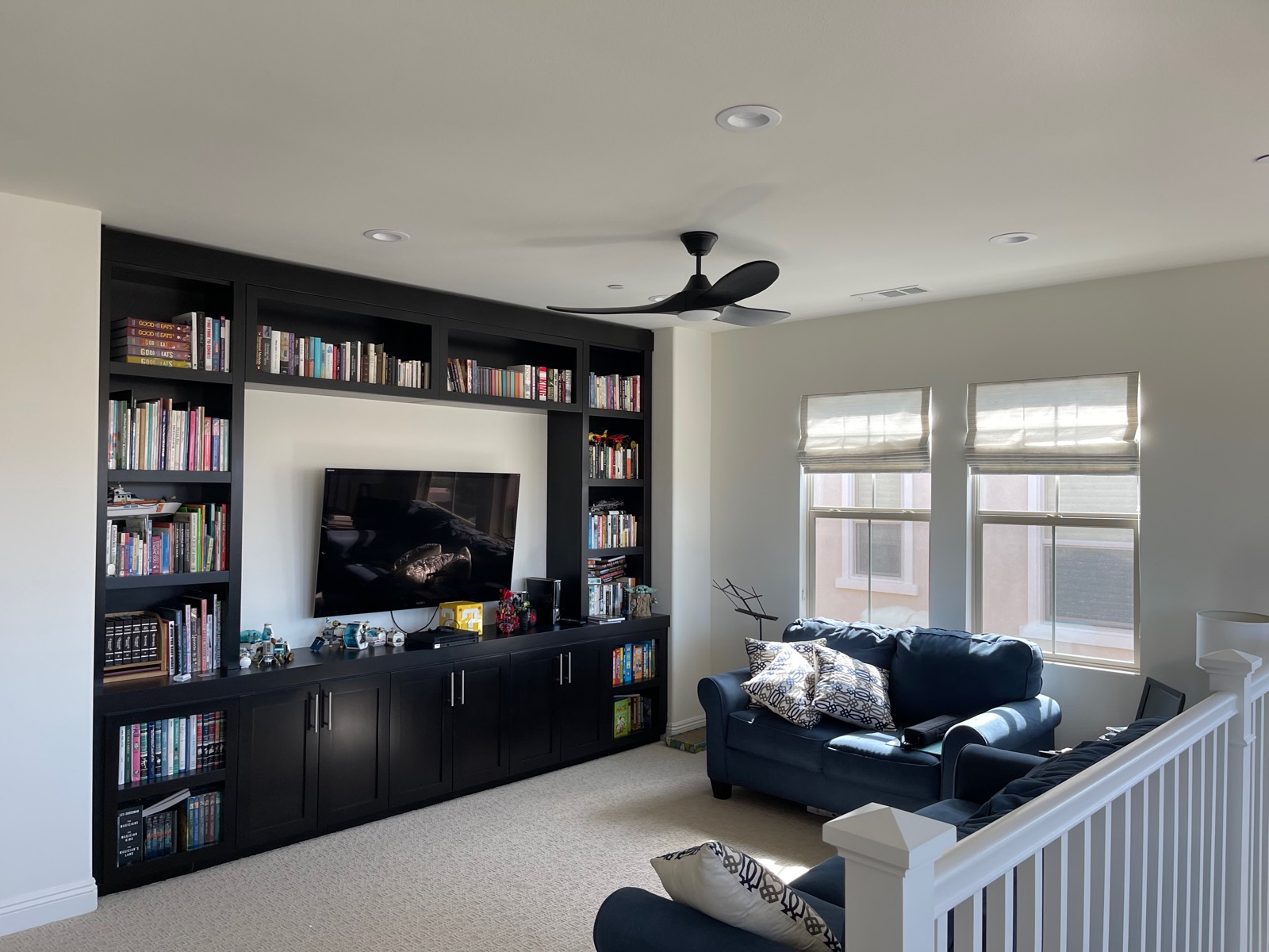 Dark three-blade ceiling fan in an upstairs loft with built-in bookshelves and a stair railing