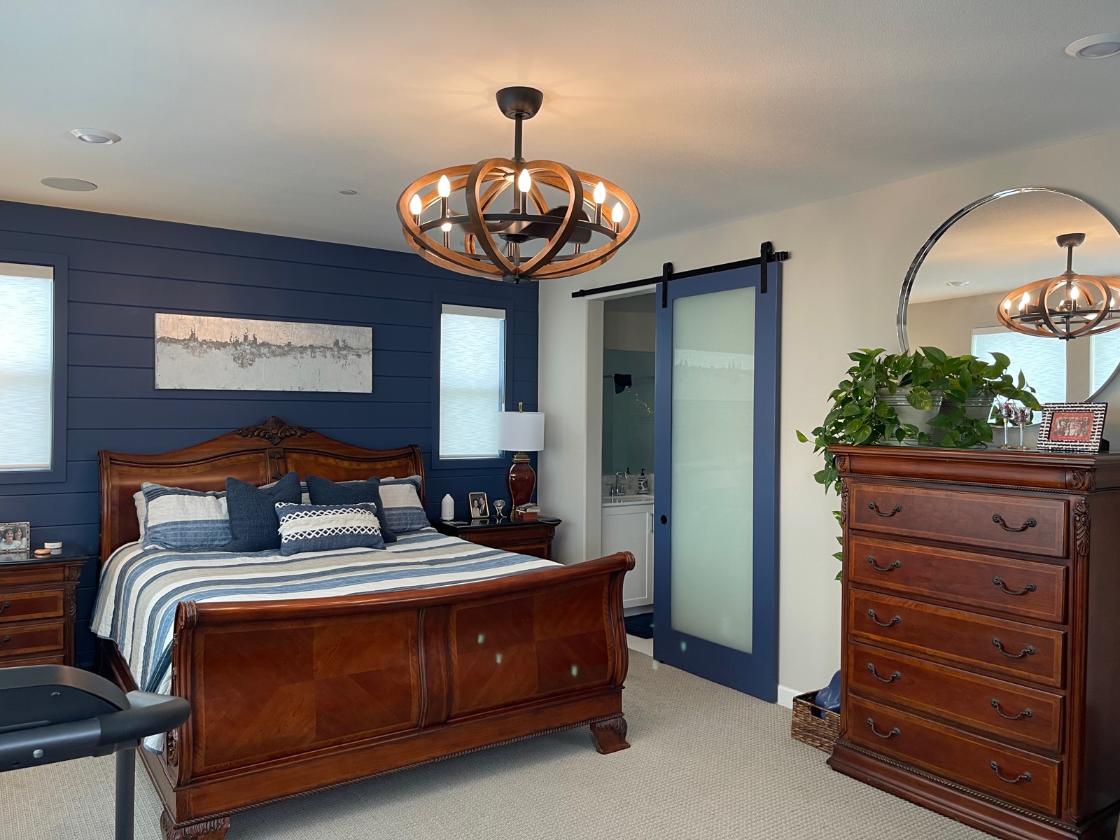 Fandelier, a ceiling fan inside a round open chandelier frame with candle-style lights, over the bed in a bedroom with a navy accent wall